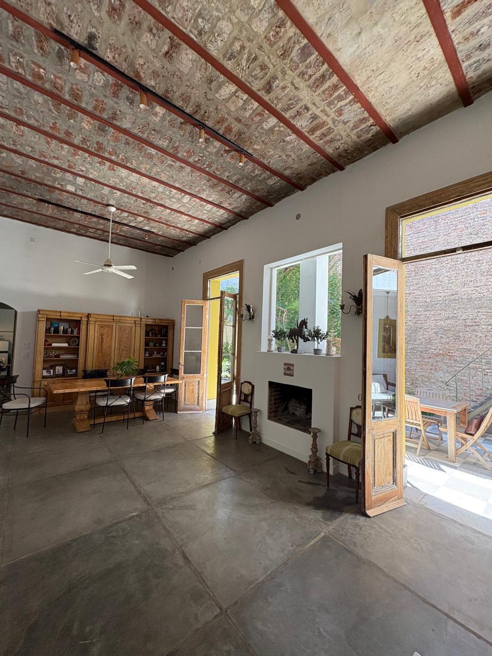 Salón interior amplio con techo de ladrillo, hogar y puertas abiertas al patio